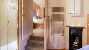 A hotel room with a bed, a bathroom with a shower, a fireplace, and a wardrobe.