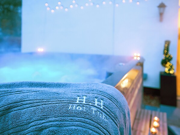 A hot tub with a towel draped over it, a string of lights in the background, and a wall-mounted lamp.