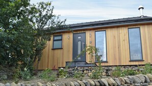 Une maison en bois avec un mur de pierre à l’avant, de grandes fenêtres et une cheminée.