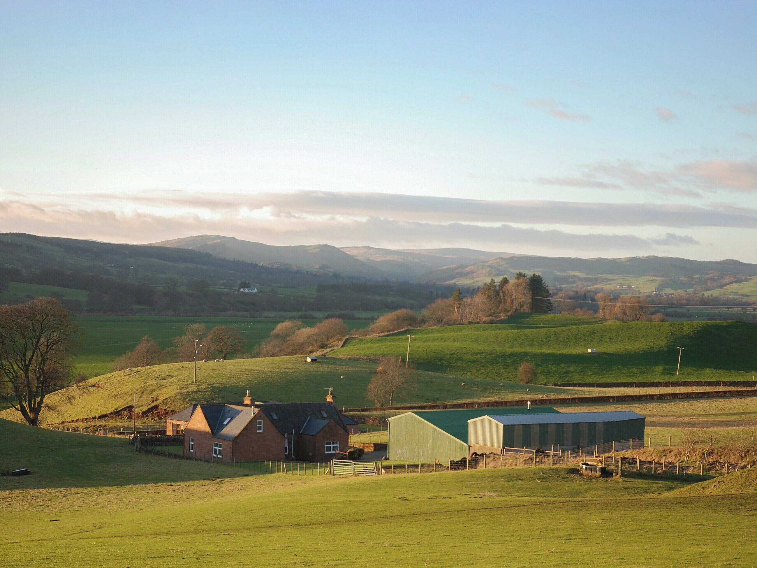 Ländliche Landschaft mit sanften Hügeln, einem Bauernhaus und einer Scheune.