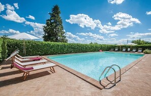 Une piscine rectangulaire, bordée d’une terrasse carrelée, entourée de chaises longues et de parasols.