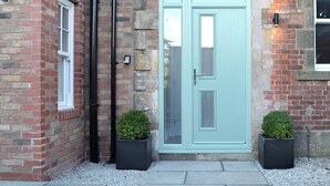 A brick building with a light blue door, two potted plants, and a window on the left.