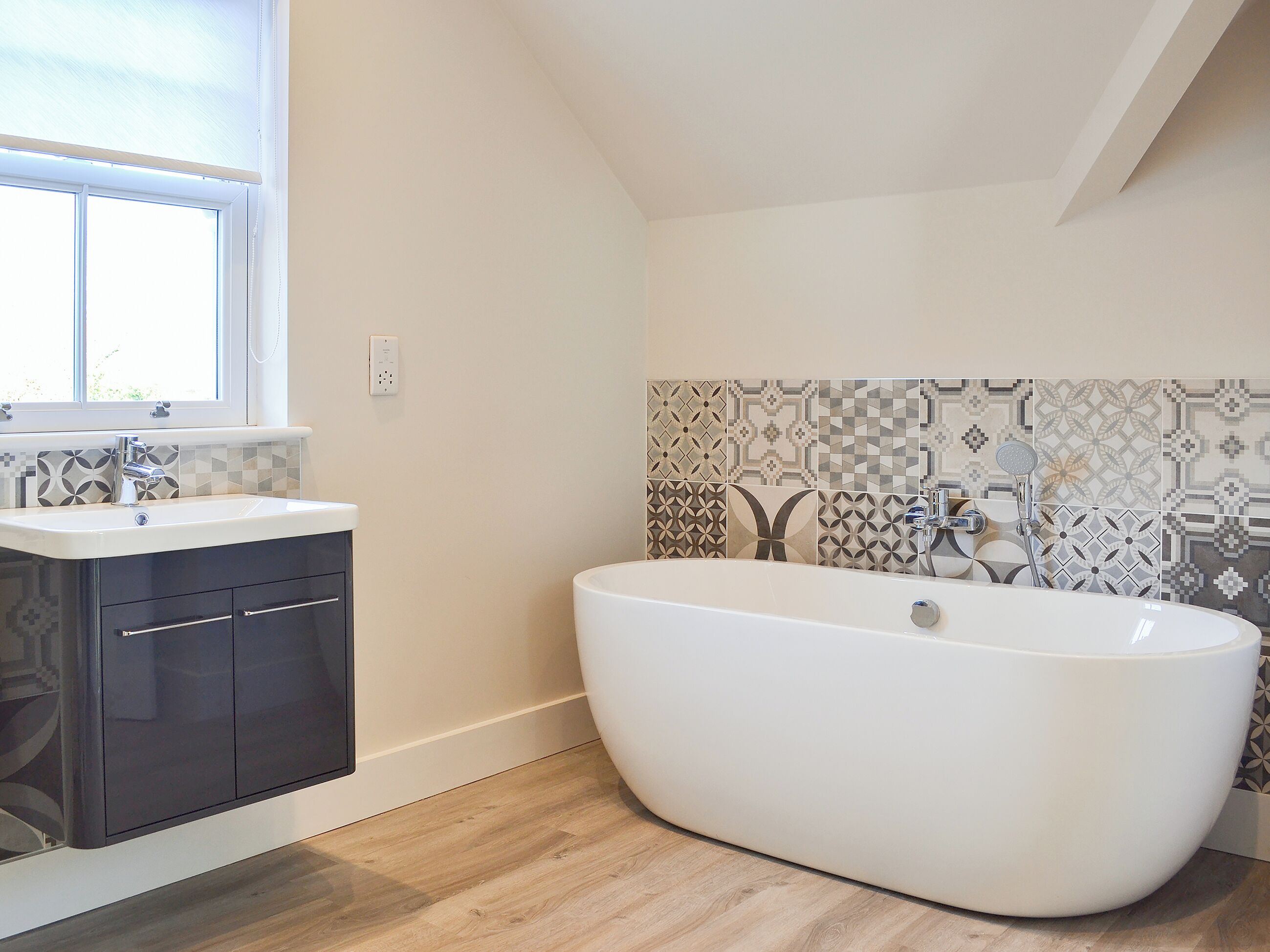 Un bagno moderno con una vasca da bagno indipendente, un mobile vanitario con pensili scuri e piastrelle decorate alle pareti.