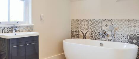 Un bagno moderno con una vasca da bagno indipendente, un mobile vanitario con pensili scuri e piastrelle decorate alle pareti.