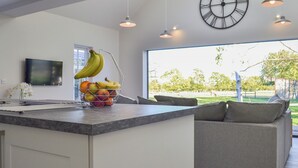 A modern kitchen with a central island, a large wall clock, pendant lights, and a view of the outdoors.