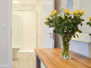 A bathroom with a toilet, a shower, and a wooden table with a vase of flowers. - 2 bedroom accommodation in Upper Poppleton, near York (Upper Poppleton, near York)