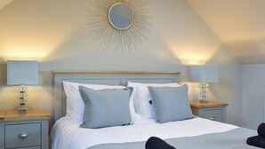 A neatly made bed with a headboard, two bedside tables with lamps, a wall-mounted mirror, and a ceiling light fixture.
