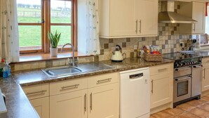 A modern kitchen with white cabinets, a built-in dishwasher, a stove, and a window with a view of a grassy field. - 5 bedroom accommodation in Bromyard, near Malvern Hills (Bromyard, near Malvern Hills)