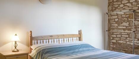 Et soveværelse med en træseng, et natbord med lampe, og en stenvæg.