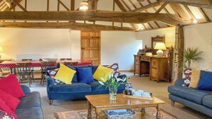 A cozy living room with a wooden ceiling, a dining area with a red tablecloth, and a blue sofa with colorful cushions. - 5 bedroom accommodation in Bromyard, near Malvern Hills (Bromyard, near Malvern Hills)