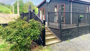 En stuga av trä med en veranda, en satellitmottagare och en liten trädgårdsyta.
