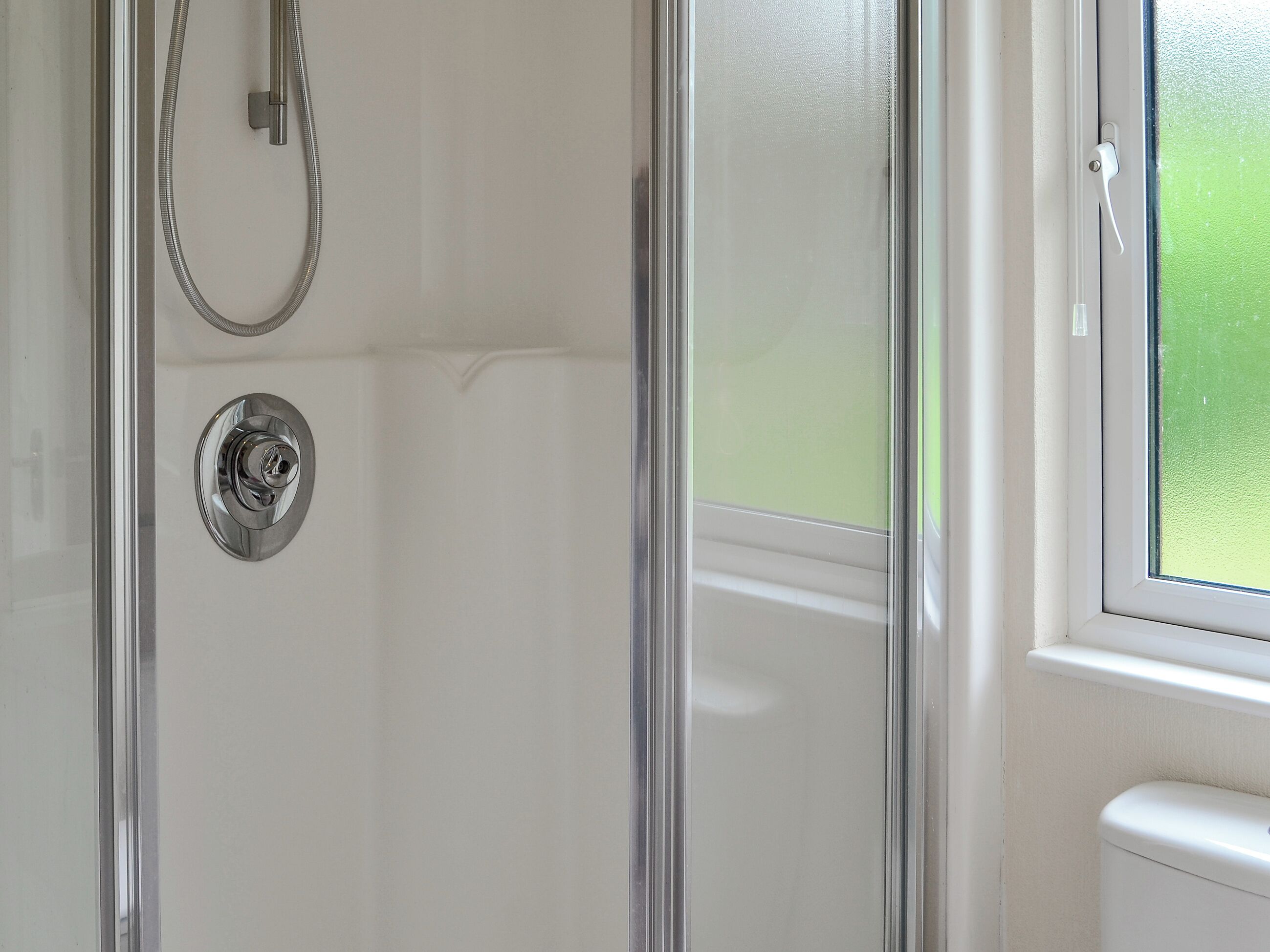 A glass-enclosed shower with a chrome faucet and a visible toilet in the adjacent room.