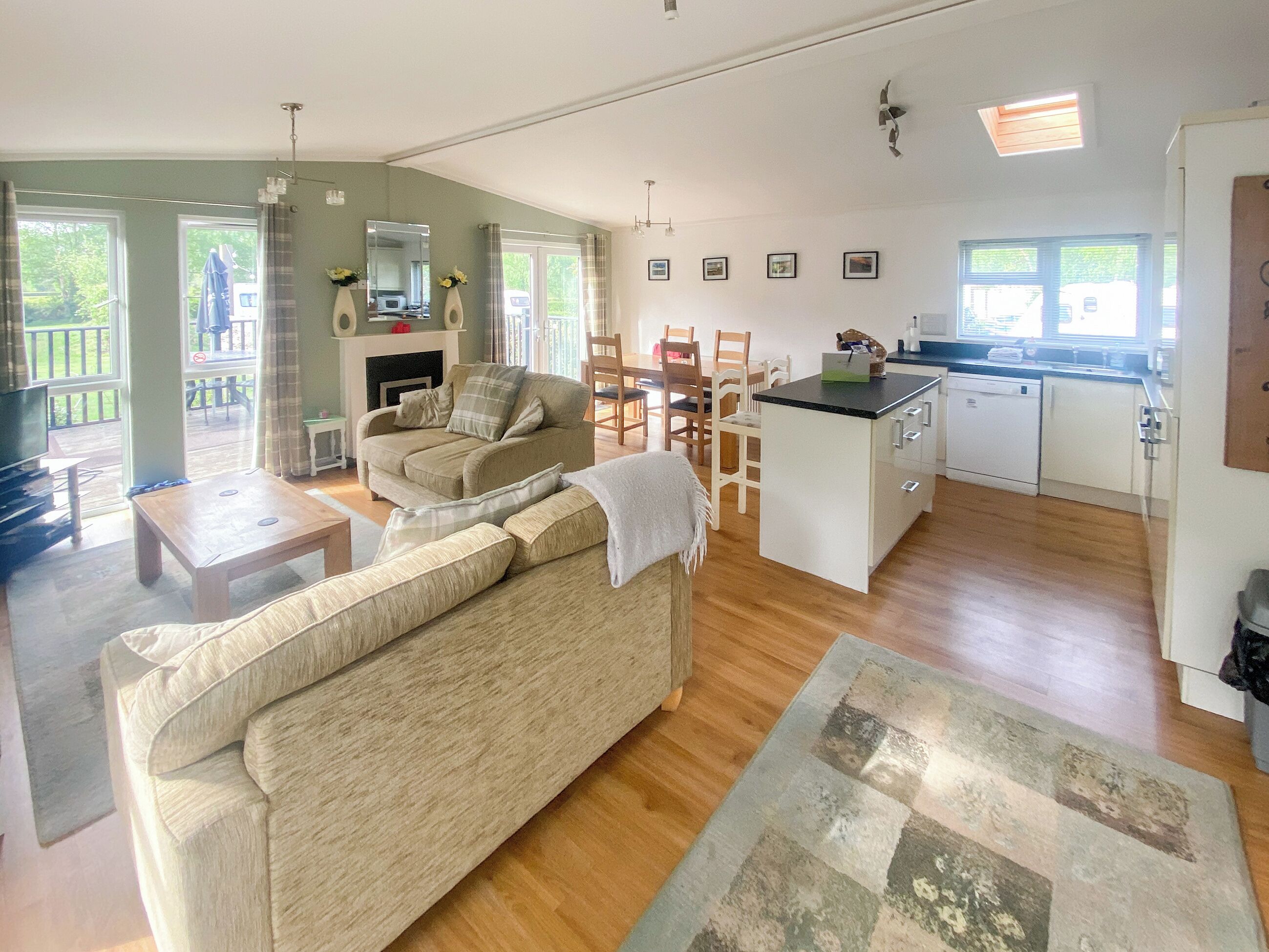 A spacious living area with a sofa, a coffee table, and a fireplace. There is a kitchen with a sink and a dining area with chairs.