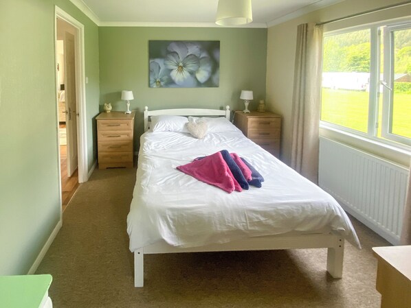 A bedroom with a bed, two bedside tables, a nightstand, a window with curtains, and a painting on the wall.