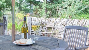 A round wooden table with a bottle of white wine, two glasses, and a plate of cheese and bread.