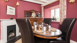 A dining room with a round table, four chairs, a fireplace, a mirror, and a window with curtains.