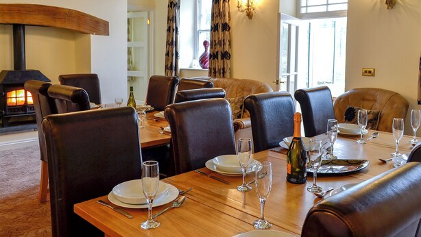 A dining area with a wooden table set for a meal, leather chairs, and a fireplace in the background. - Maesbangor Farmhouse (Capel Bangor, near Aberystwyth)