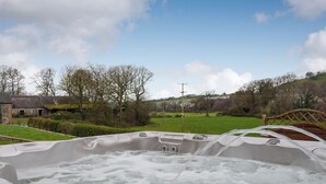 A hot tub with a view of a rural landscape, including a wooden bridge and a stone building. - Maesbangor Farmhouse (Capel Bangor, near Aberystwyth)