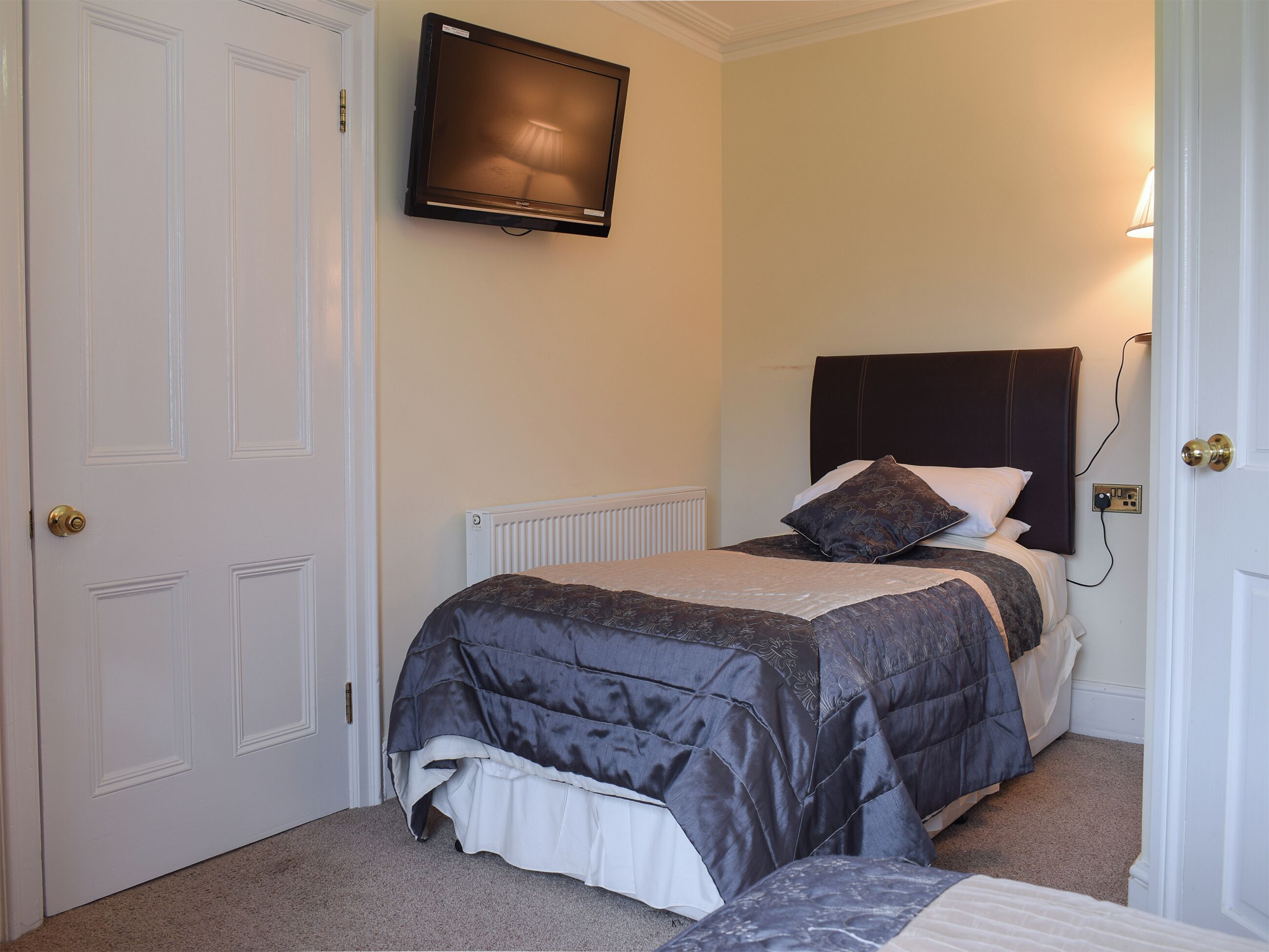 A bedroom with a bed, a television mounted on the wall, and a door.