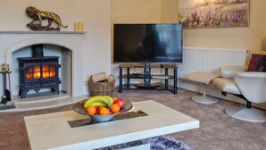 A living room with a fireplace, a flat-screen TV, a comfortable sofa, and a fruit bowl on a coffee table. - Maesbangor Farmhouse (Capel Bangor, near Aberystwyth)