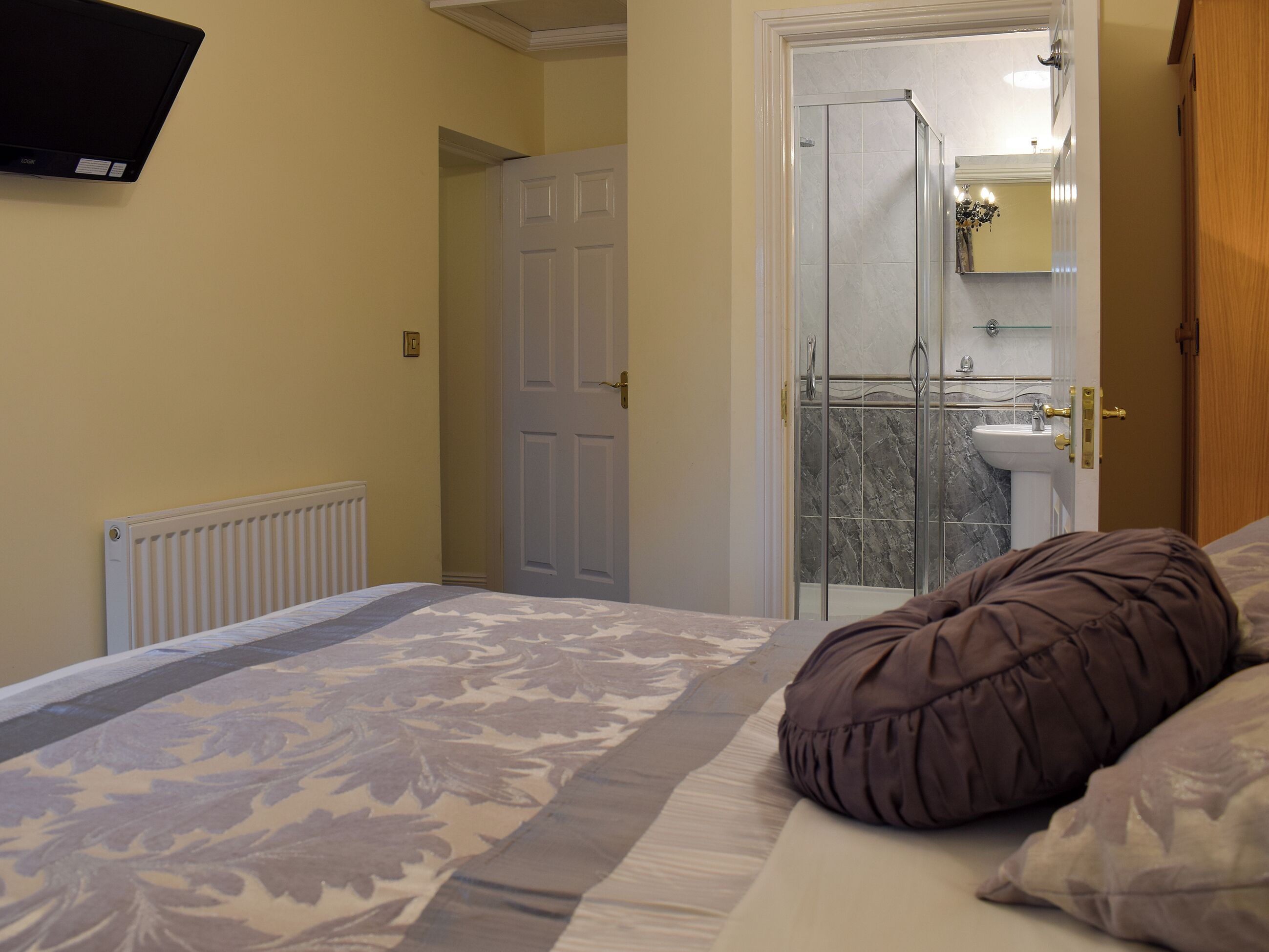 Un dormitorio con cama, un radiador, una puerta y un baño visible a través de un cristal.
