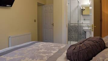 Un dormitorio con cama, un radiador, una puerta y un baño visible a través de un cristal.