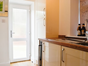 Een keuken met een witte deur, houten kastjes en een aanrecht met twee flessen.