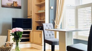 A living room with a television, a grey armchair, a table, and a bookshelf. - 1 bedroom accommodation in Whitby (Whitby)