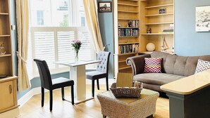 A cozy living room with a sofa, a coffee table, a bookshelf, and a dining area with chairs and a table. - 1 bedroom accommodation in Whitby (Whitby)