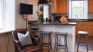 A kitchen with wooden cabinets, a black range hood, a microwave, and a window with a view. There is a chair and two stools in the corner. - 3 bedroom accommodation in Fortingall, near Aberfeldy (Fortingall, near Aberfeldy)