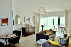 A modern living room with a sofa, a dining table, and a cabinet. There is a large window with curtains, and a view of the outside.