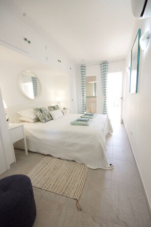 Ein Schlafzimmer mit einem Bett, einem runden Spiegel, einem Nachttisch und einem Fenster mit Vorhängen.