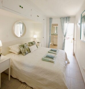 A bedroom with a bed, a bedside table, a mirror, and a view of the bathroom.