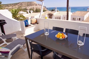 Ein Balkon mit Tisch, Stühlen, einer Obstschale und Blick auf das Meer und Gebäude.