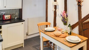 A kitchen with a wooden table set for two, a toaster, and a vase with flowers. - Lavenham Red Brick Cottage (Lavenham)