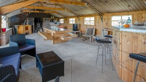Un interior rústico de madera con una zona de bar, asientos y una cocina visible a través de una puerta abierta.