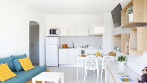 A modern, compact living space with a kitchenette, a dining area, and a sofa with cushions.