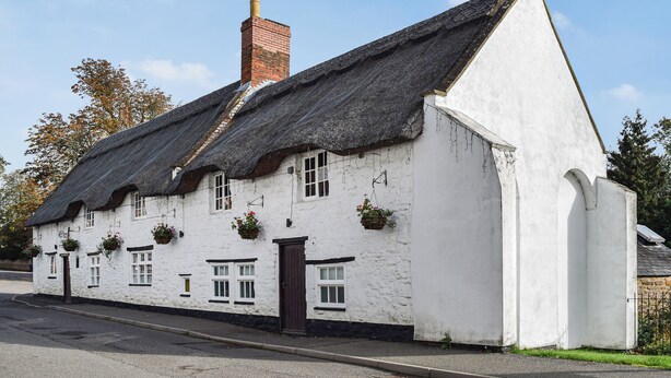 A traditional white building with a thatched roof, multiple windows, and hanging flower baskets. - 2 bedroom accommodation in Welton (Welton)