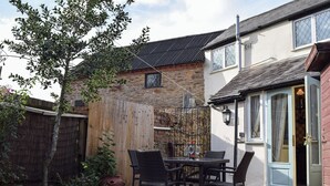A patio with a table and chairs, a wooden fence, and a building with a door and windows. - 2 bedroom accommodation in Welton (Welton)