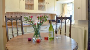 A dining area with a round table, chairs, a vase with flowers, a wine bottle, and glasses. - 2 bedroom accommodation in Welton (Welton)
