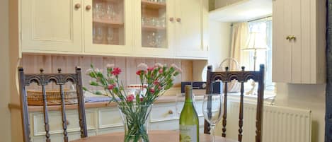 A dining area with a round table, chairs, a vase with flowers, a wine bottle, and glasses.