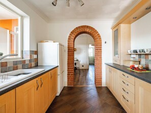 Uma cozinha com armários de madeira, um arco de tijolos, uma geladeira e uma bancada com legumes.