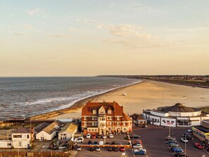A coastal hotel with a parking lot, beach view, and adjacent buildings.