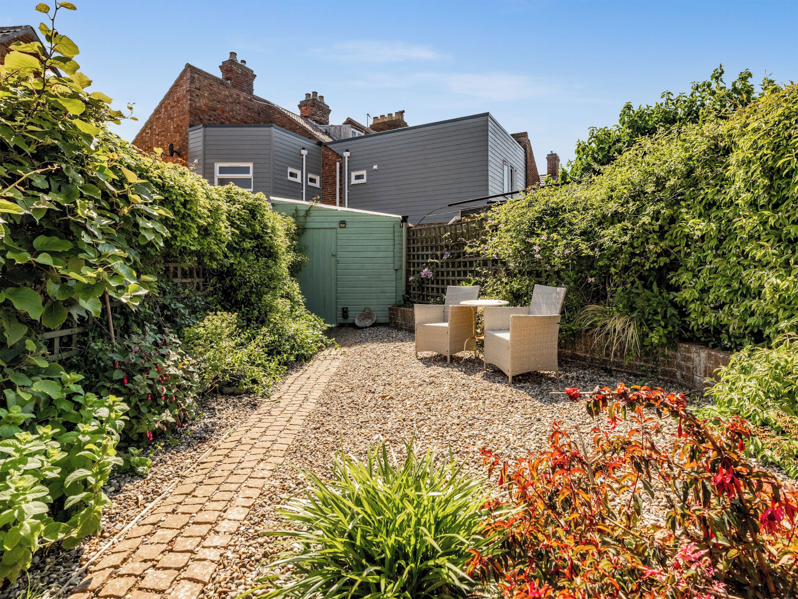 A garden with a paved pathway, a green shed, and outdoor furniture.