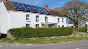 A white two-story house with a solar panel roof, a stone chimney, and a well-maintained hedge. - 3 bedroom accommodation in Rhossilli, near Swansea (Rhossilli, near Swansea)