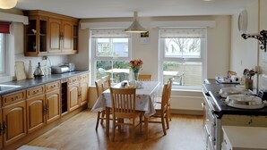 A kitchen with wooden cabinets, a dining table with chairs, a window with a view of the outside, and a stove. - 3 bedroom accommodation in Rhossilli, near Swansea (Rhossilli, near Swansea)