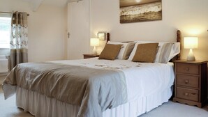 A bedroom with a bed, two bedside tables with lamps, a door, and a painting on the wall. - 3 bedroom accommodation in Rhossilli, near Swansea (Rhossilli, near Swansea)