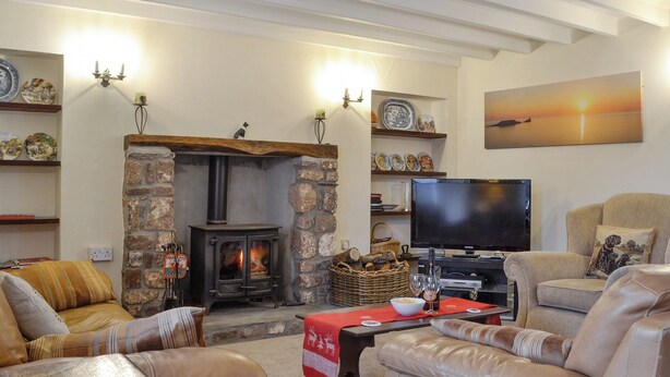 A cozy living room with a stone fireplace, leather sofas, a television, and decorative plates on shelves. - 3 bedroom accommodation in Rhossilli, near Swansea (Rhossilli, near Swansea)