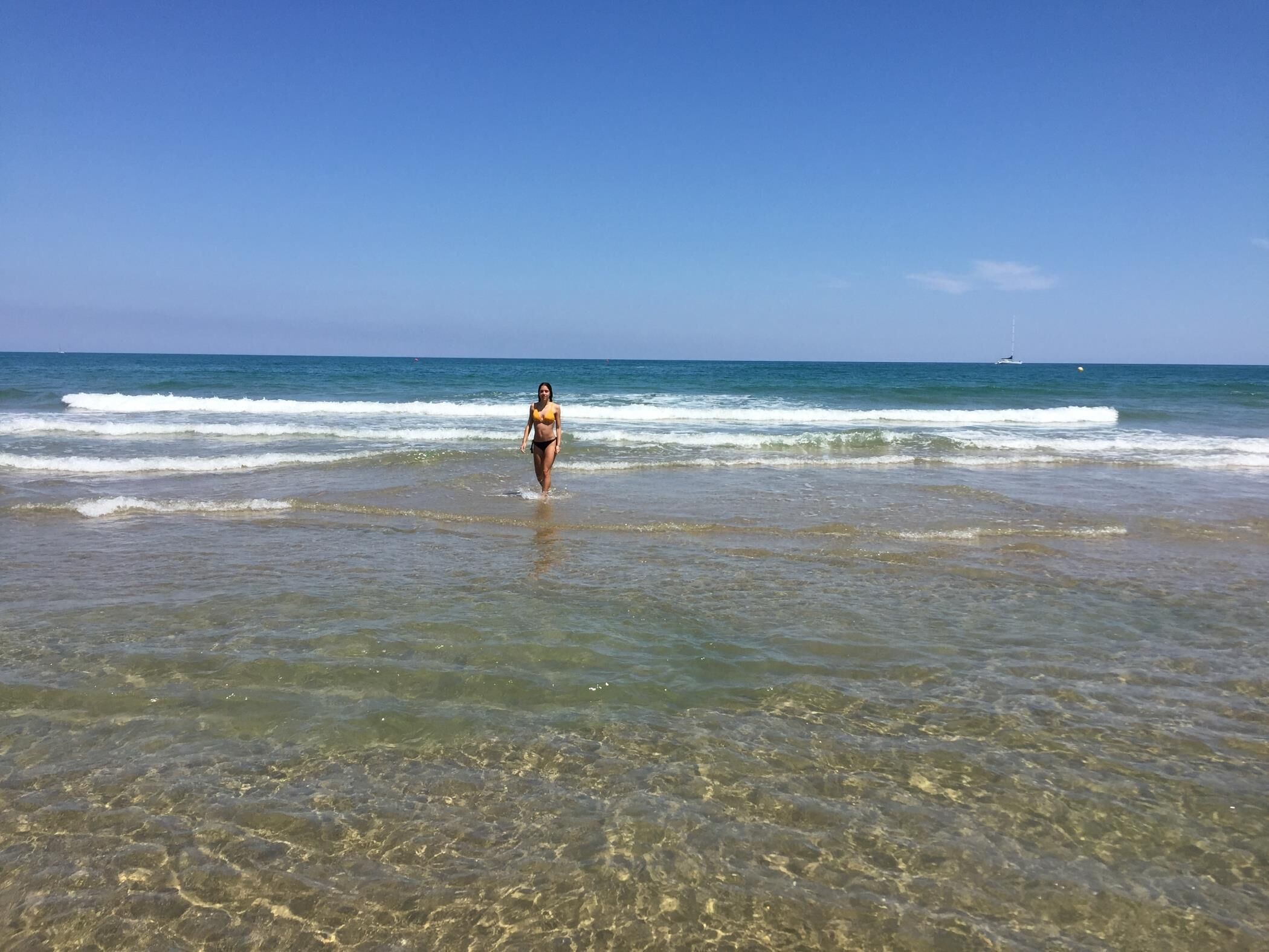 A beach scene with clear shallow waters and a person walking towards the ocean.