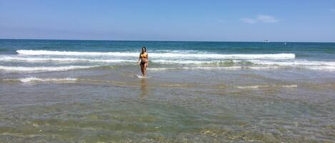 A beach scene with clear shallow waters and a person walking towards the ocean.
